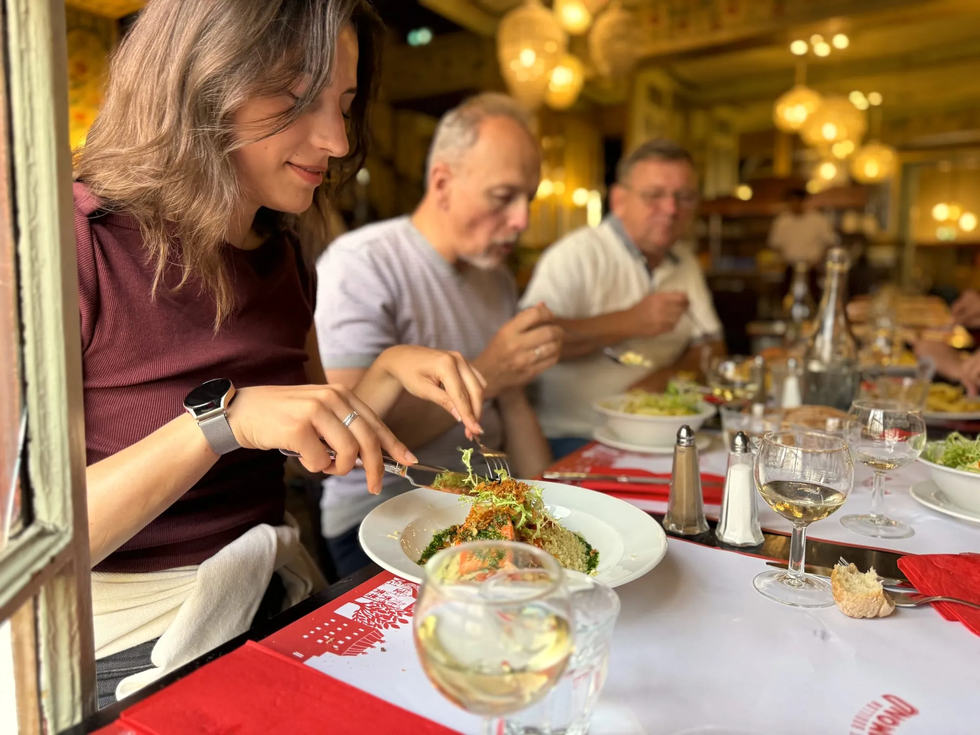 A group eating lunch at a warm classic Parisian brasserie, wine poured, plates full