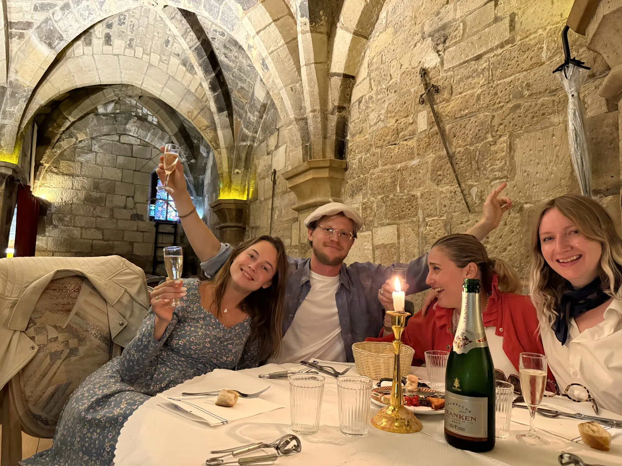 Four guests toasting with champagne by candlelight in a medieval stone cellar
