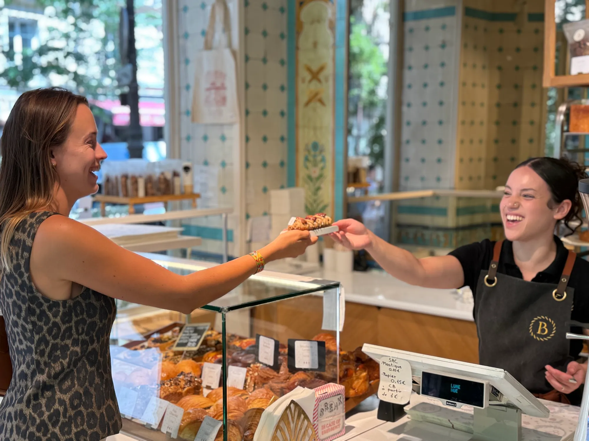 A baker handing a wrapped parcel across the counter to a guest