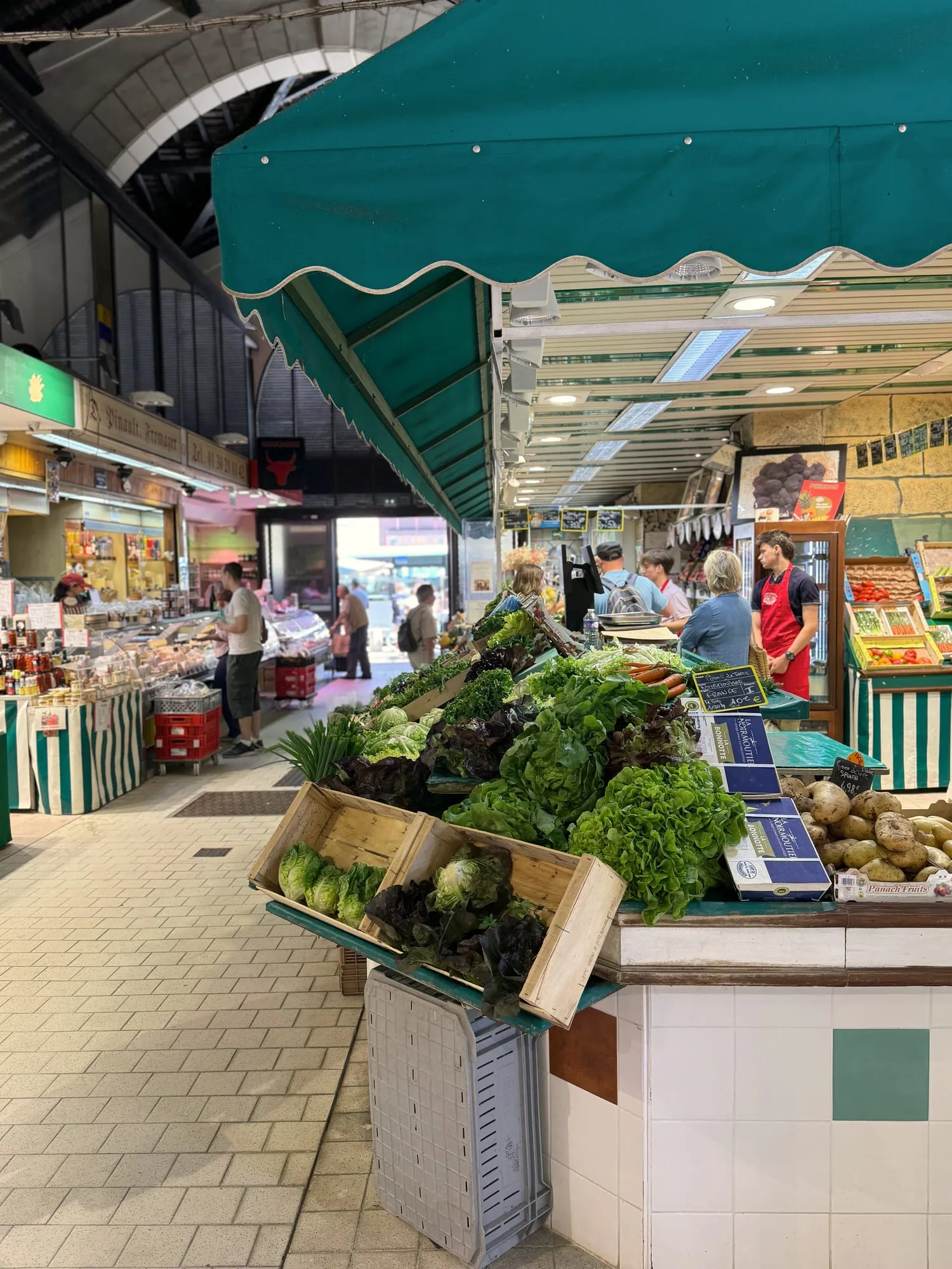 Fresh lettuces and vegetables piled under a green awning inside a covered market