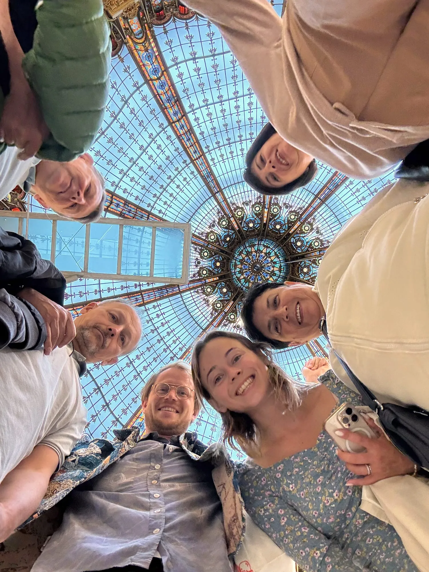 Six guests in a circle smiling down at the camera under a stained glass dome