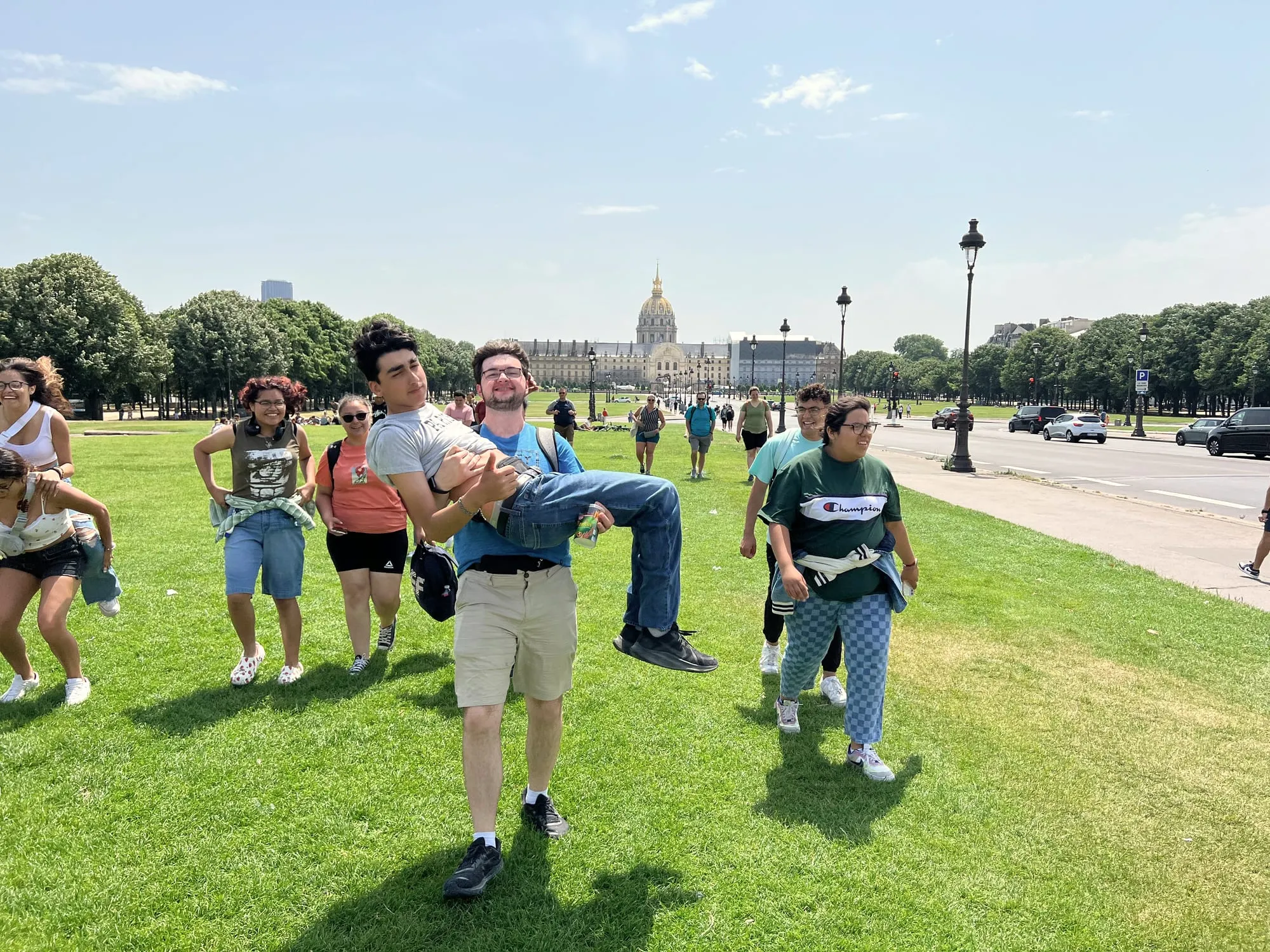 A group of young travelers goofing around on a lawn in front of Les Invalides