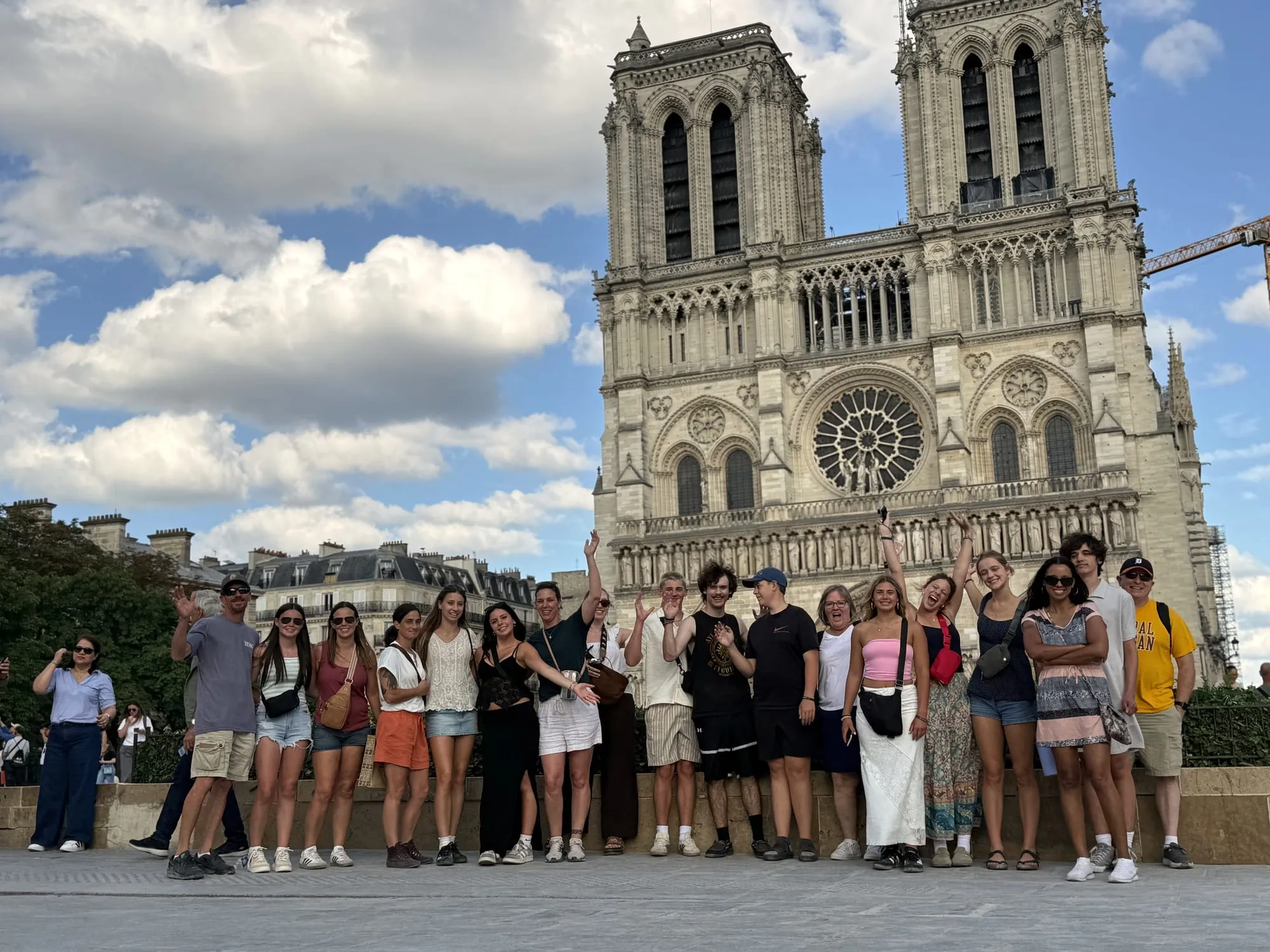 A large tour group waves in front of the towers and rose window of Notre-Dame