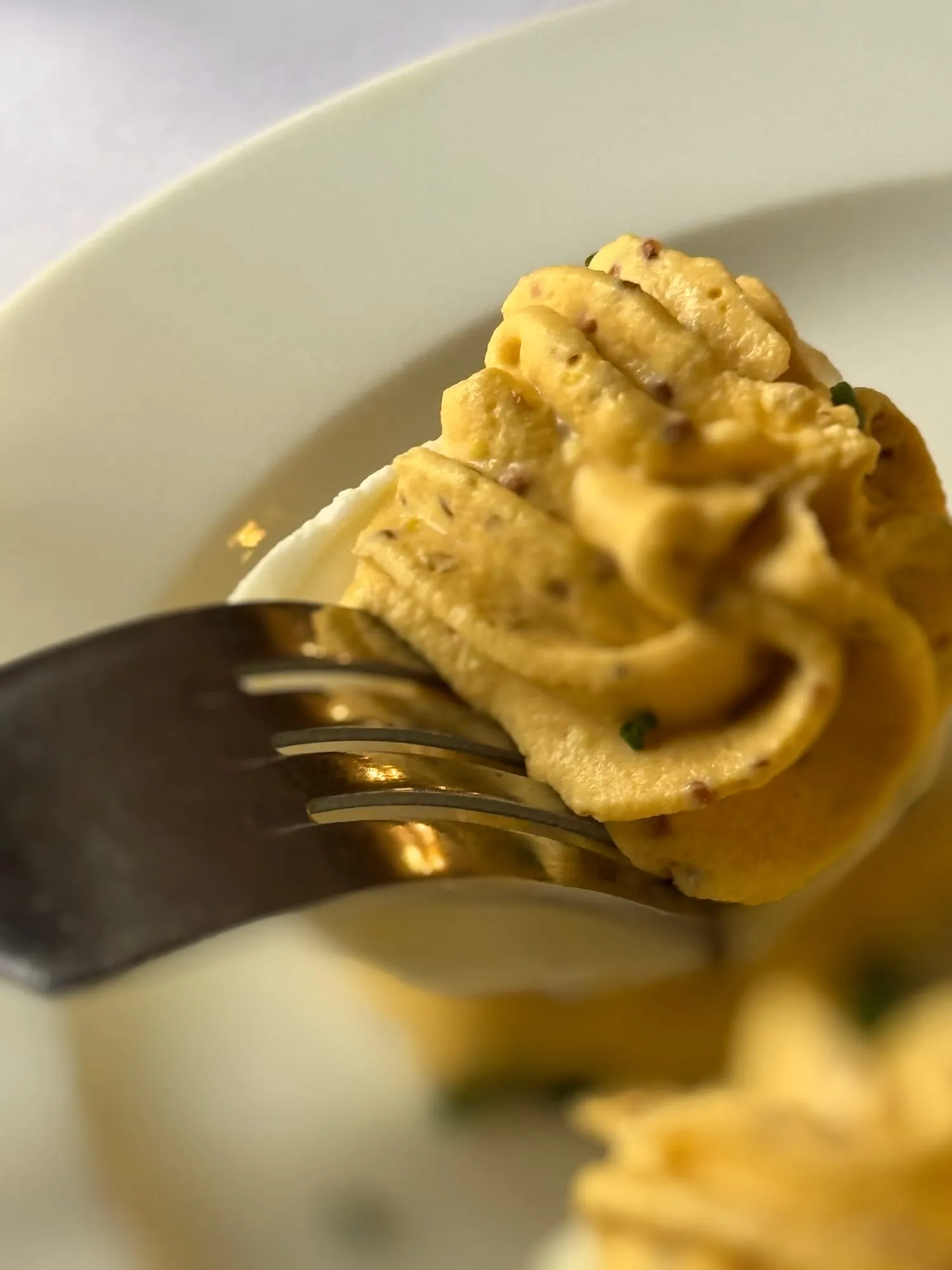 Fork lifting a bite of oeuf mimosa, a classic French deviled egg with piped filling