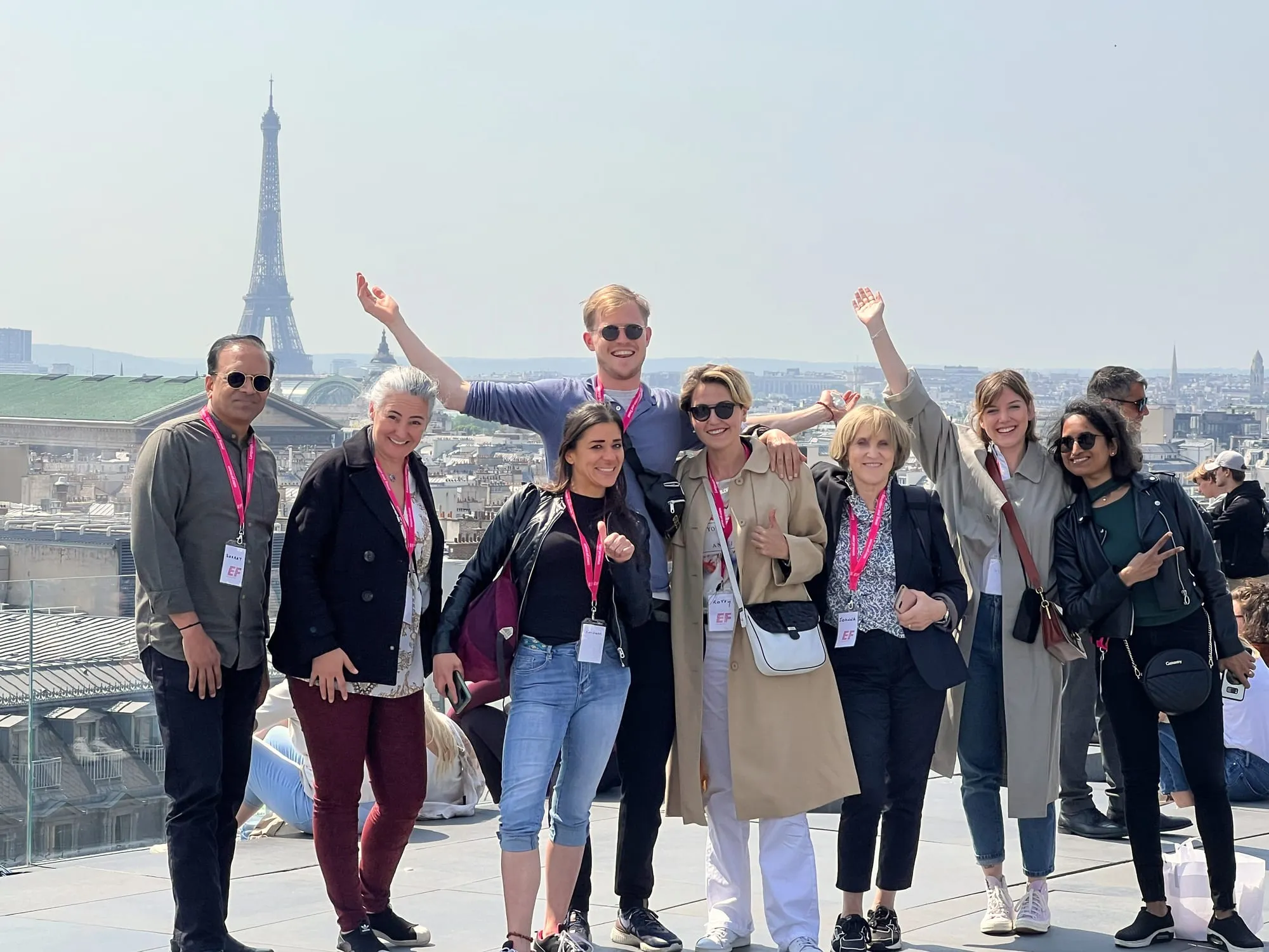 Eight guests with arms raised on a rooftop terrace in Paris, the Eiffel Tower behind them