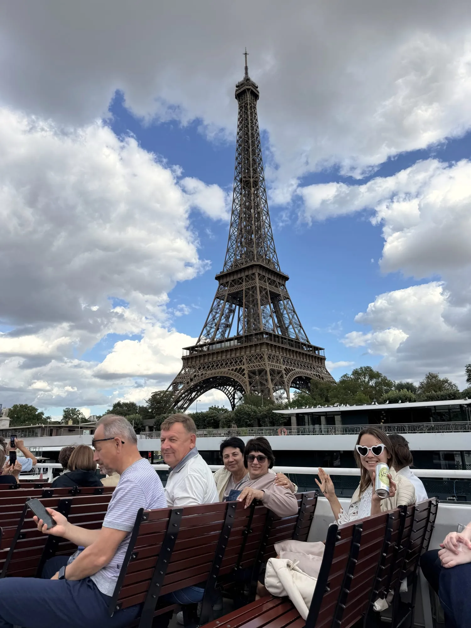 Passengers on an open-air Seine cruise boat with the Eiffel Tower behind